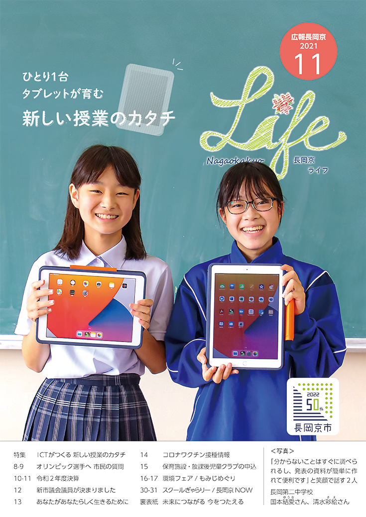 長岡京ライフ2021年11月号の表紙。中学校の黒板の前で、生徒2人がタブレットを持って笑っている写真。